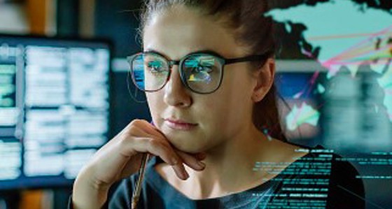 A woman looking thoughtful in front of multiple computer screens