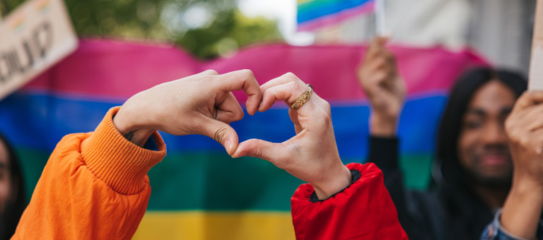 2 hands making a heart in front of rainbow flag