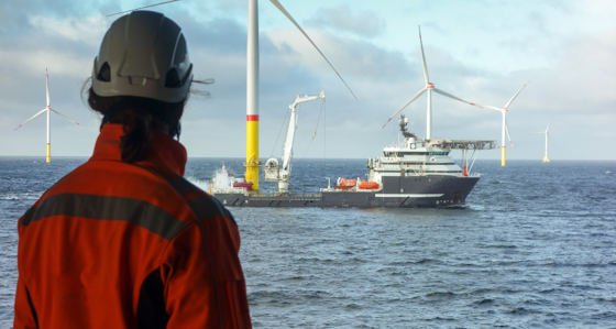 Worker looking towards a ship in an offshore wind farm