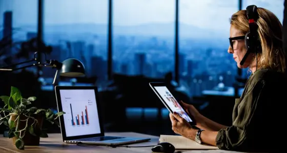 Woman in an office looking at reports on her laptop and tablet