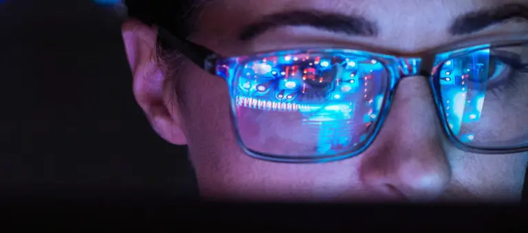 Woman in a dark room with screen monitor reflecting in her glasses