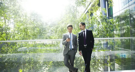 Two men looking at a phone while standing on a balcony in front of trees