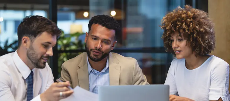 Three colleagues discussing plans in front of a laptop