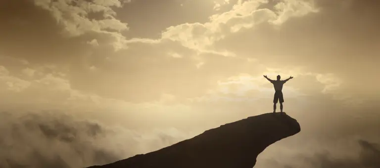 Man extending his arms on top of a cliff