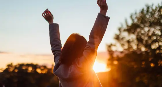 Rear view of young woman stretching arms against sunset in the sky